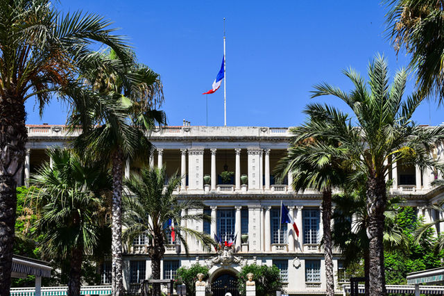 Elegant French colonial-style building surrounded by palm trees in Nice, France.