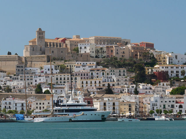 Beautiful view of Ibiza's historic Dalt Vila with yachts anchored in the harbor and a clear blue sky.