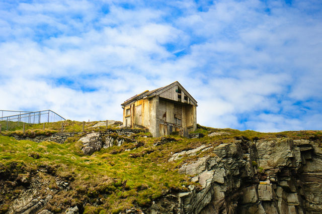 Old abandoned building on a rocky, grassy hill.