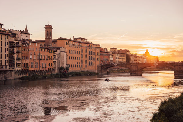Beautiful sunset over Ponte Vecchio in Florence, Italy, casting warm hues on the Arno River.