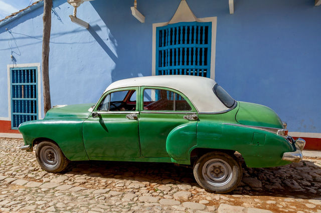 Vintage green car parked on a cobblestone street in Camagüey, Cuba, with colorful colonial architecture.
