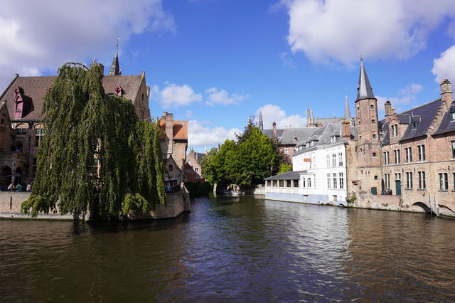 Picturesque canal scene with historic architecture in Bruges, Belgium under a blue sky.
