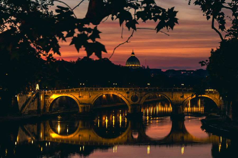 Sunset Bridge Reflecting On River, Golden Arches Lit, Domed Silhouette Beyond, Treeframed Foreground, Glassy