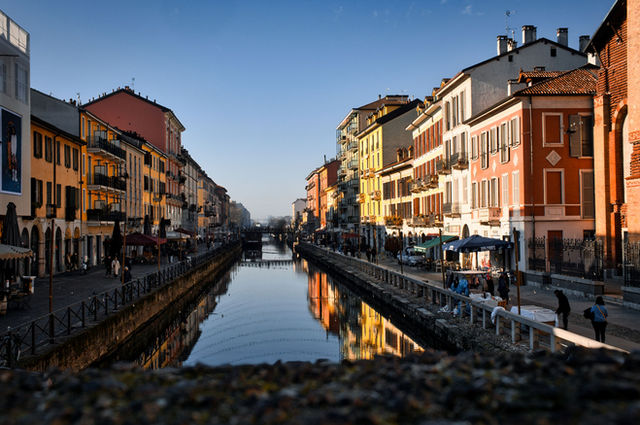 Charming scene of outdoor cafes and colorful buildings lining a canal in Milan's Navigli District.