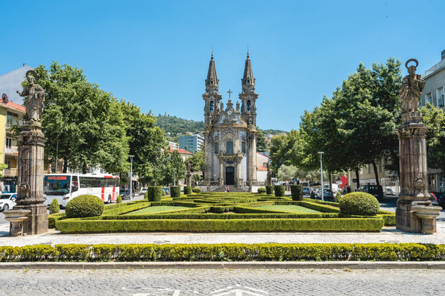 Sunlit view of Nossa Senhora da Consolação Church in Guimarães, Portugal, surrounded by lush gardens.