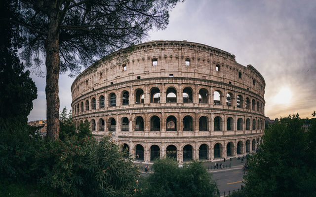 Captivating wide-angle shot of Rome's iconic Colosseum with a serene sunset backdrop.