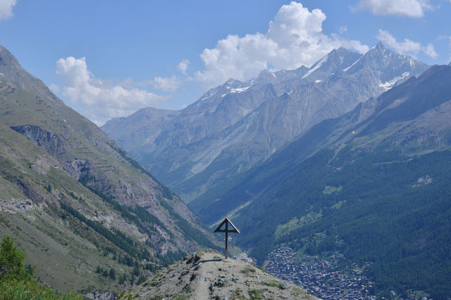 A symbolic cross pointing towards the sky, with an alpine village