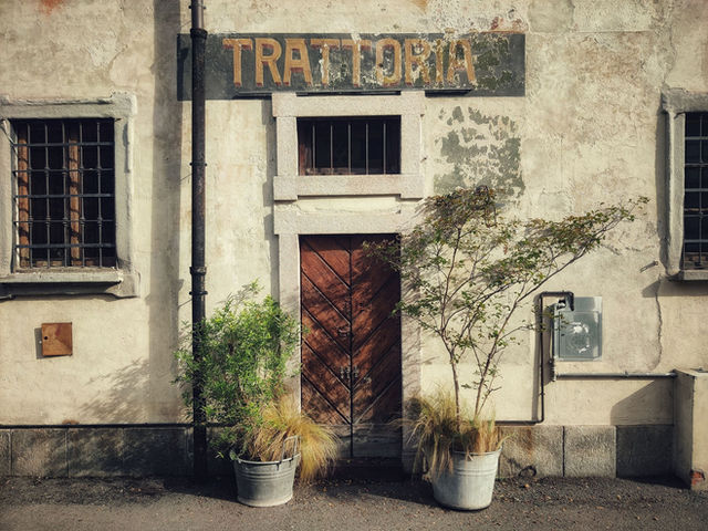 Vintage Italian trattoria entrance with rustic wooden door and potted plants in Milan's urban scene.