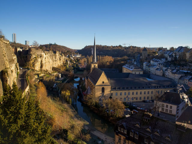 A picturesque view of Luxembourg's cityscape featuring a historic church, canal, and blue sky.