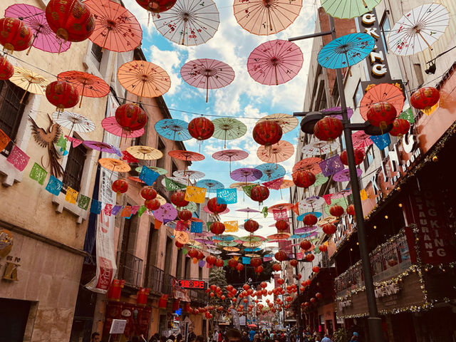 Colorful paper umbrellas and red lanterns hanging above a narrow street in Mexico City