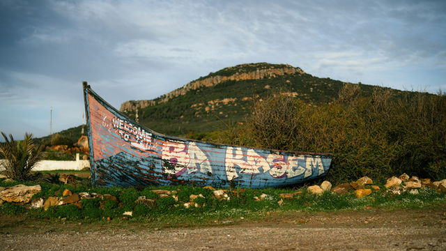 Graffiti-covered boat rests on grassy landscape near hill