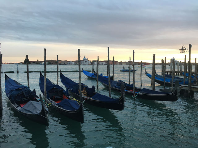 Gondolas docked on the Grand Canal in Venice at sunset, showcasing a serene view of the iconic city.