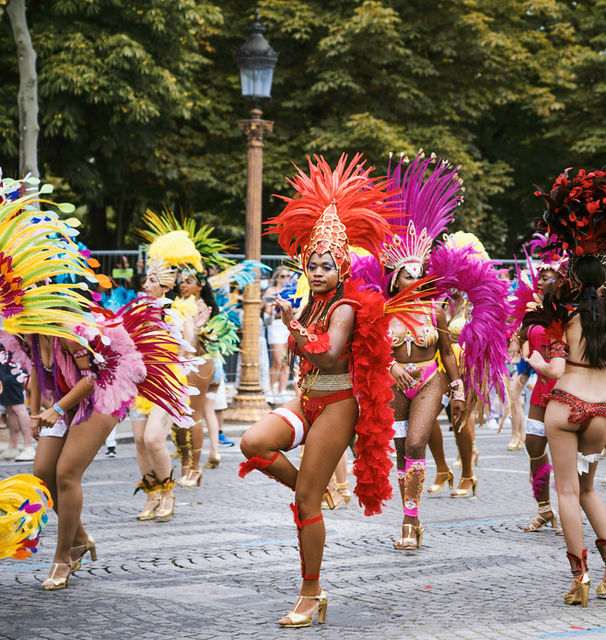 A samba line mid-step on the cobbles, feathers in every colour