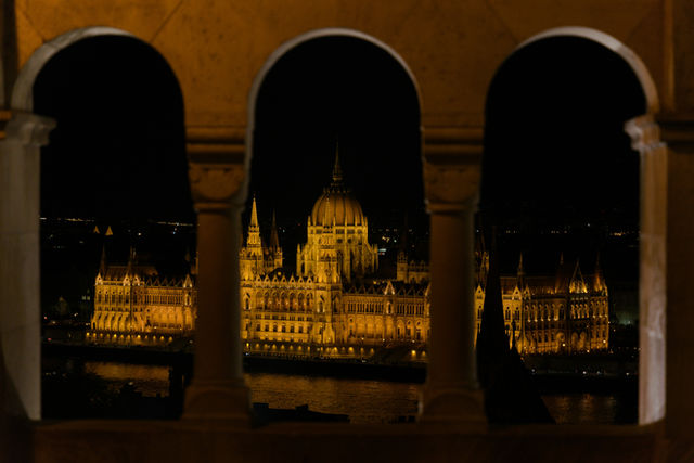 Illuminated grand building seen through three arched windows at night.
