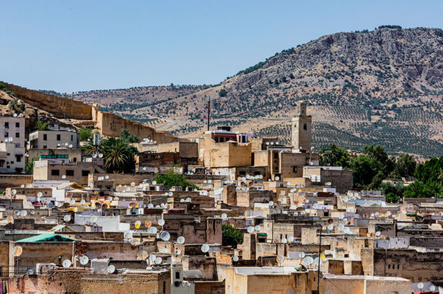 Explore the vibrant rooftops of Fes with satellite dishes, against a backdrop of Moroccan mountains.