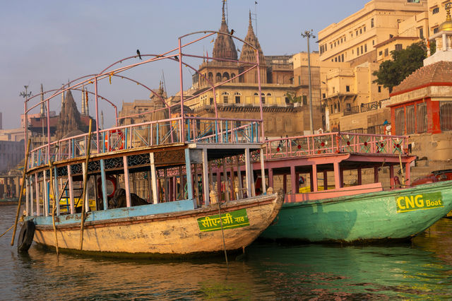 🚣 Boats Moored Along the Ghats – Varanasi, India This evocative image features a couple of wooden boats gently resting in the waters near the ghats of Varanasi, Uttar Pradesh. Bathed in soft sunset li