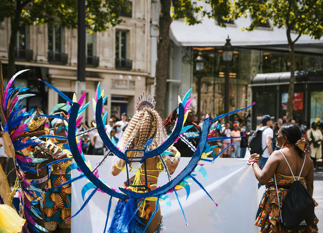 Blue wings and a braided crown, seen from behind on a Haussmann boulevard — the Paris tropical carnival
