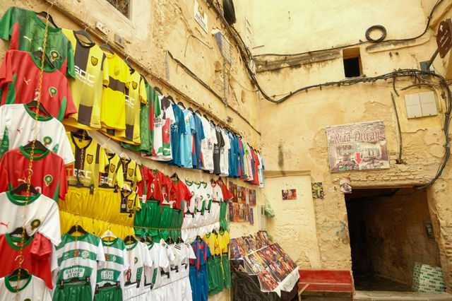 A vibrant display of soccer jerseys in an old street market in Fes, Morocco.