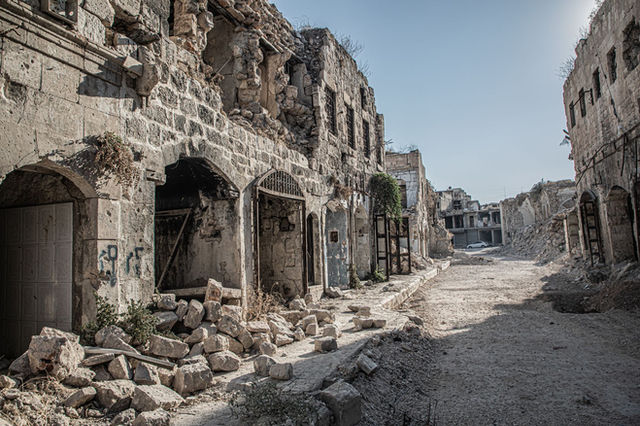 A deserted, war-torn street in Aleppo, captured in daylight, showcasing destruction and desolation.