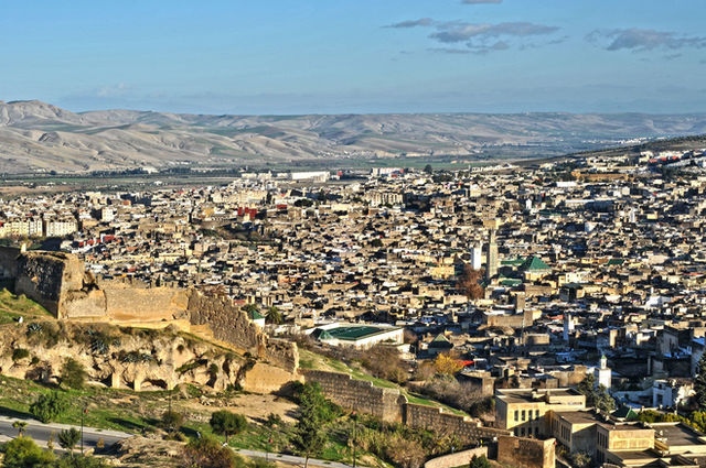 A vibrant aerial view of Fes, Morocco, displaying the ancient city's architecture against the Atlas Mountains.
