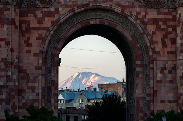 Snow-capped mountain seen through an arched stone structure.