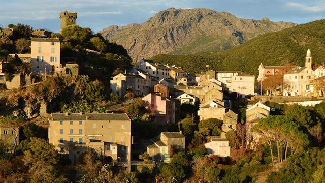 Scenic view of Nonza village in Corsica surrounded by mountains and lush greenery.