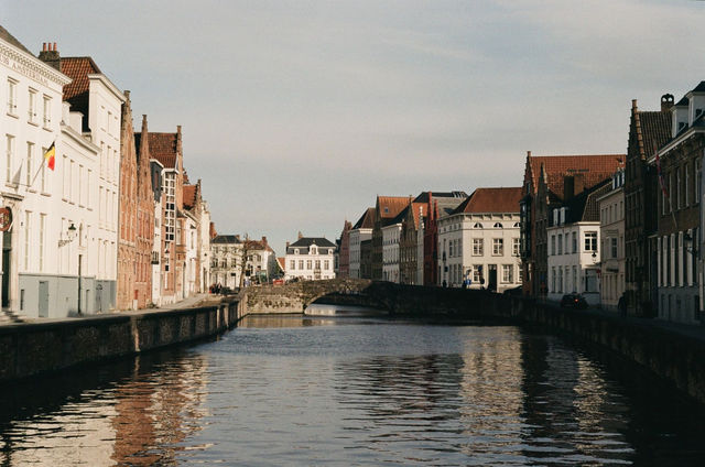 Scenic view of Bruges canal and historic Flemish buildings under clear sky.