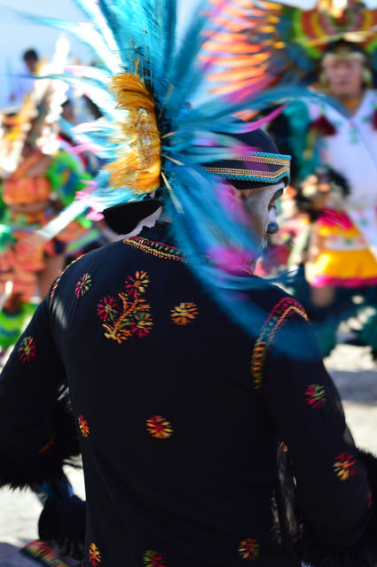 Turquoise plumes over an embroidered blouse — a danzante in procession