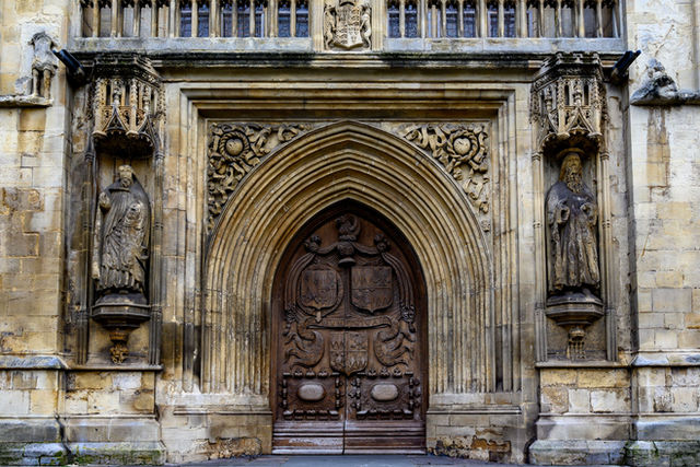 Ancient Gothic entrance of Bath Abbey with intricate stone carvings and wooden door.