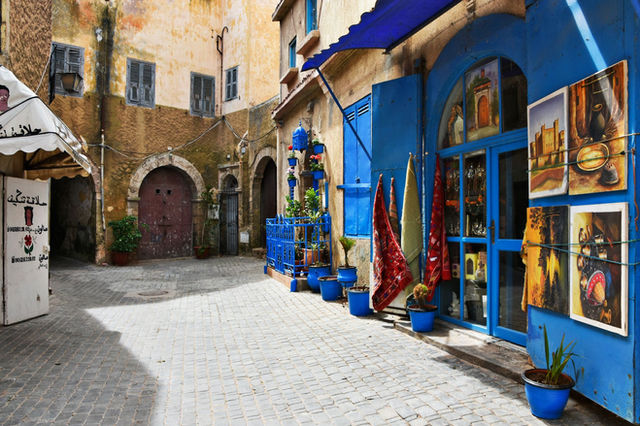 Explore a vibrant alleyway in El Jadida, Morocco, featuring colorful art, blue accents, and cozy shops.