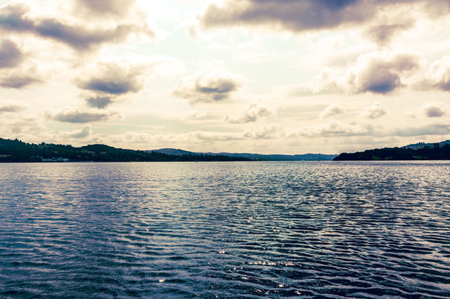 Peaceful Lake Windermere scene with calm waters and dramatic clouds in the scenic Lake District, England.
