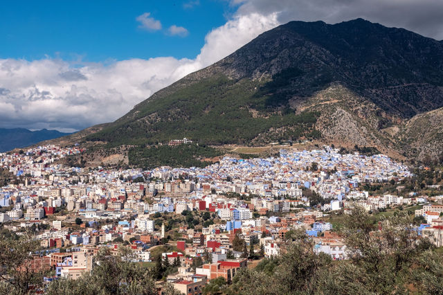 Panoramic view of the vibrant blue city of Chefchaouen in Morocco under a dramatic sky.