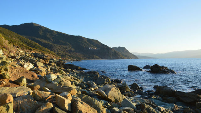 Scenic view of the rocky coastline at Ogliastro, Corsica, during sunset with serene ocean waves.