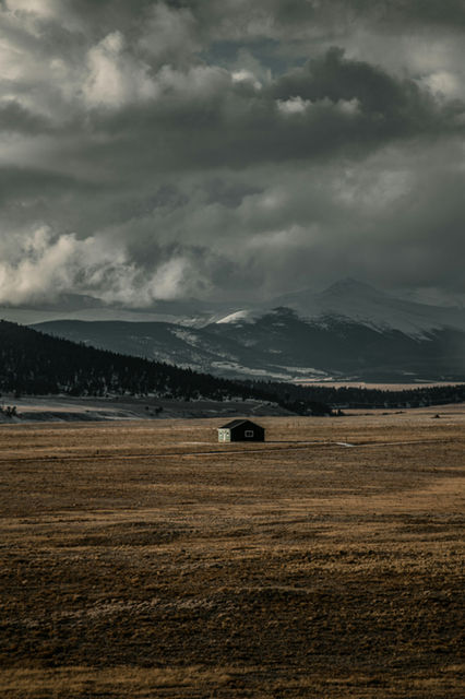 a field with a barn and mountains in the background