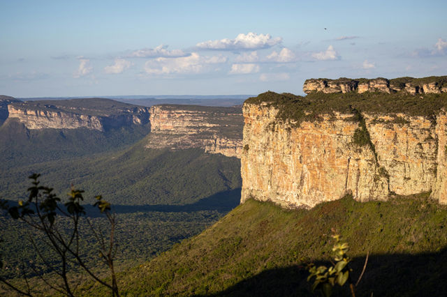 Layered sandstone cliffs overlook a lush green valley.