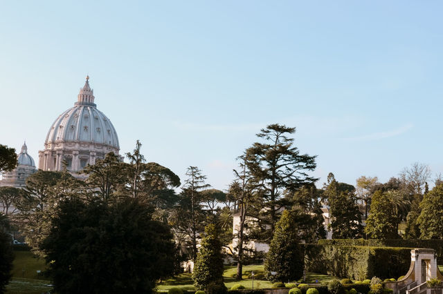 Scenic view of St. Peter's Basilica dome peeking over lush Vatican Gardens.