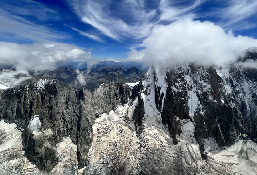 Aerial of the Mont Blanc massif's granite spires and hanging glaciers under streaming cirrus, Chamonix