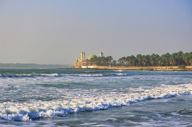 Waves crash on a beach near a domed building.