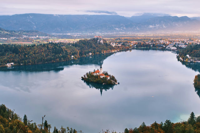 Lake with island church and distant mountains at dawn