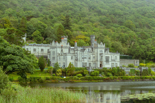The historic Kylemore Abbey set against lush green hills and reflected in a calm lakeside scene.