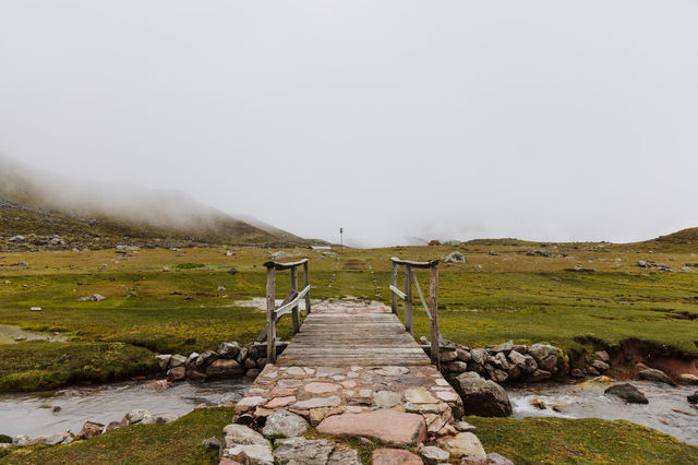 A serene footbridge crossing a stream in the misty countryside of Cusco, Peru.