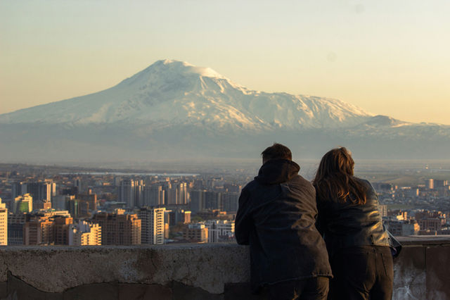 Couple looking at a snow-capped mountain over cityscape.