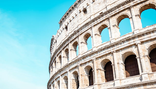 Close-up of the iconic Colosseum in Rome, bathed in sunlight and set against a vibrant blue sky.