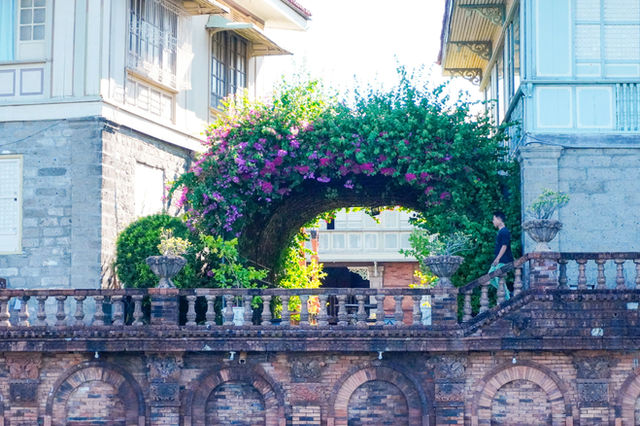 Lush floral archway over a decorative stone wall.