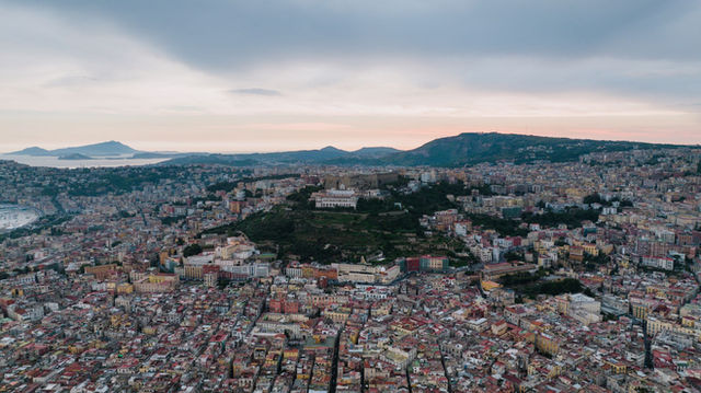 Stunning aerial view of Naples, Italy, showcasing its vibrant cityscape and surrounding mountains at dusk.