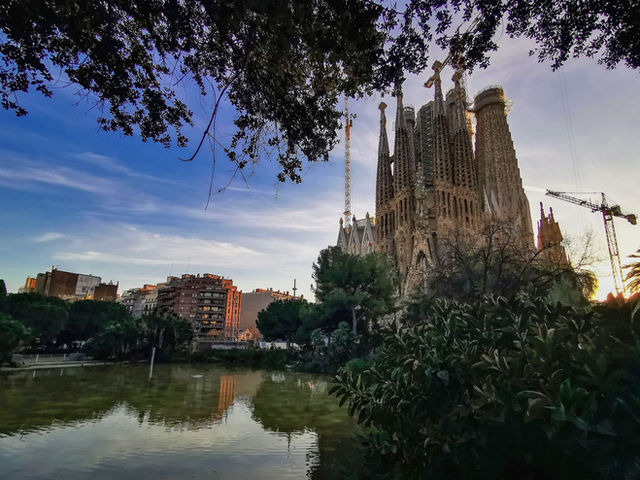 Capture of the iconic Sagrada Familia in Barcelona at sunset with reflections on a nearby pond.