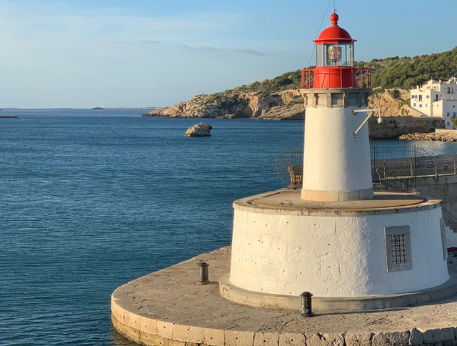 Picturesque lighthouse on Ibiza's coastline with clear blue sea and rocky landscape.