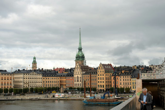 The historic skyline of Gamla Stan in Stockholm, featuring the elegant spire of the German Church (Tyska kyrkan) under a dramatic overcast sky.