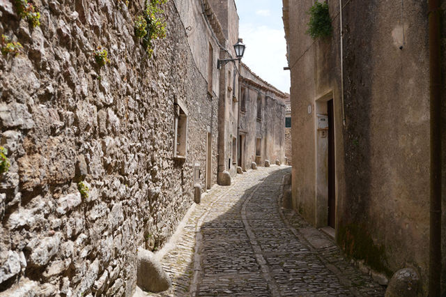 Explore a quaint cobblestone street surrounded by historical stone buildings in Erice, Sicily.