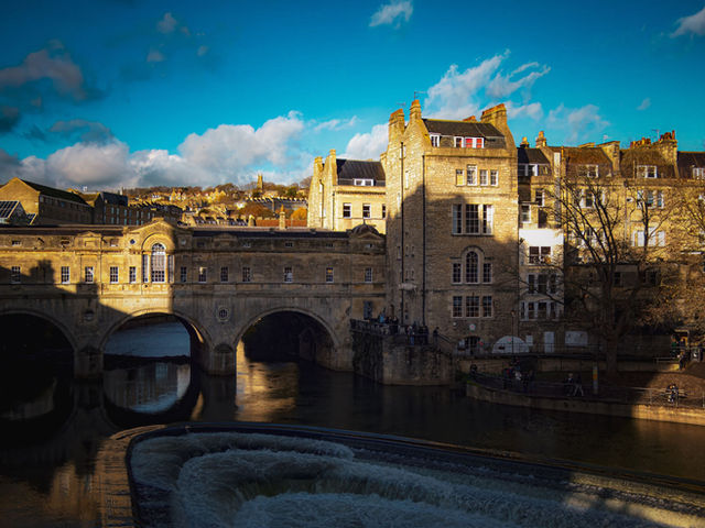 A picturesque view of the historic Pulteney Bridge in Bath, captured on a sunny day with clear blue skies.
